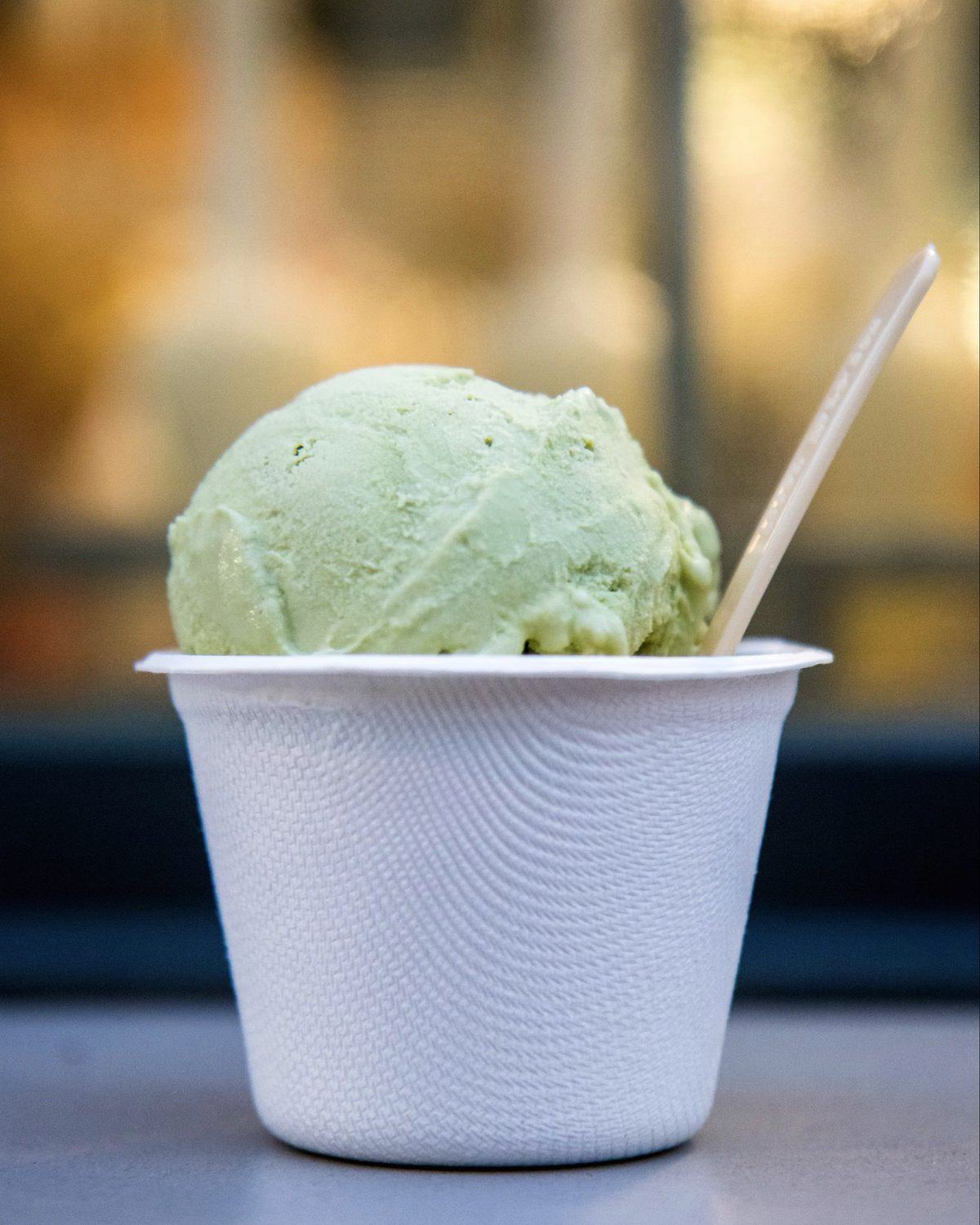 A scoop of pistachio ice cream in a paper cup on a counter
